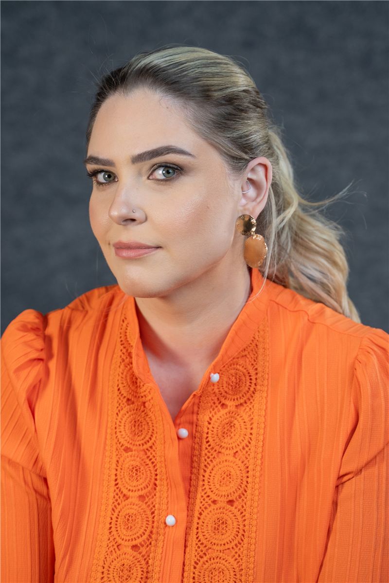 Raphaela Spellmeier de blusa laranja, olhando para a câmera